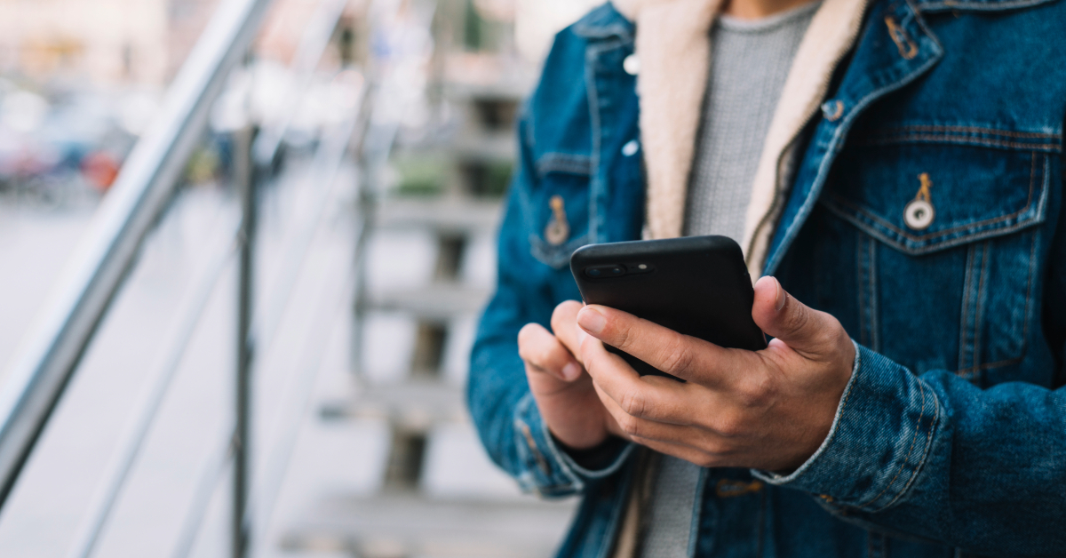 Homem usando roupas de frio segurando um celular com campanha de SMS para vendas no inverno